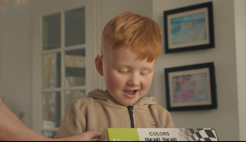 Een jong kind met rood haar kijkt blij naar een kleurrijke doos van een RC Auto.