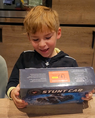 Jongentje bekijkt enthousiast doos met stunt RC auto aan tafel in keuken Race Auto